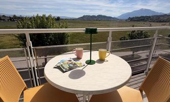A cozy table with two chairs on a balcony. In the background, a landscape stretches out with mountains and a blue sky.