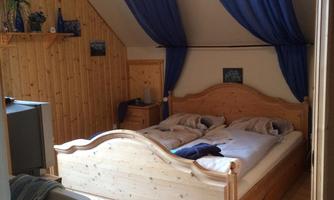 A cozy bedroom with a wooden bed and blue curtains. The walls are made of wood, and there is a television nearby.