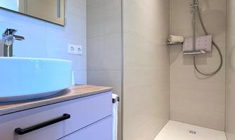 A modern bathroom with a walk-in shower and a sink. The walls and the floor are in light color tones.