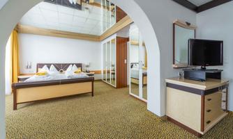 A modern hotel room with a double bed and two pillows. The room has large windows with curtains and a flat-screen television.