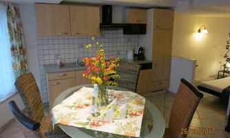 A cozy kitchen with a glass dining table and fine flowers. The room is bright and friendly with modern furniture.