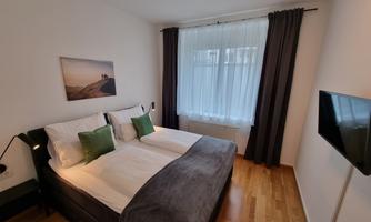 A modern bedroom with a large double bed and comfortable linen. The walls are light, and the windows are decorated with curtains.