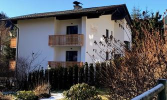 A modern house with balconies in a quiet setting. The garden is green and well-kept, surrounded by trees and shrubs.
