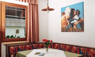 A cozy room with a table and a bench. On the wall hangs a picture of a child with a cow.
