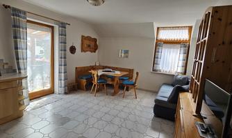 A bright living space with a cozy dining area and a sofa. Large windows provide plenty of daylight.
