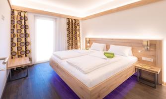 A modern bedroom with a large double bed and wooden details. Large windows provide plenty of light and a cozy atmosphere.