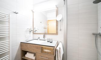A modern bathroom with a wooden vanity, mirror, and shower. Towels are neatly arranged on the table.