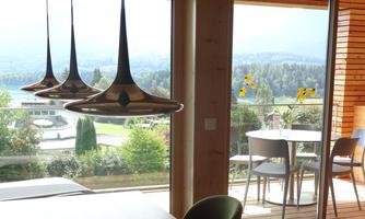A modern interior with a view of a green landscape and a lake. Chairs are at the table and a vase with sunflowers.