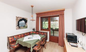 A cozy kitchen with a dining area and a view of nature. The table is nicely set, and the room is bright and inviting.