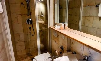 A modern bathroom with a glass shower and bright marble. The amenities include a toilet and a vanity with a wooden surface.
