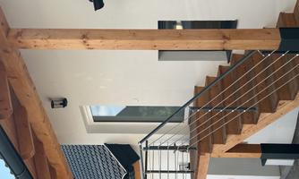 A modern house with a wooden porch and metal railing. The staircase leads to the front door under a clear sky.