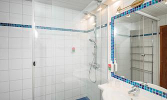 A modern bathroom with a shower cubicle and a sink. The walls are decorated with white tiles and blue accents.