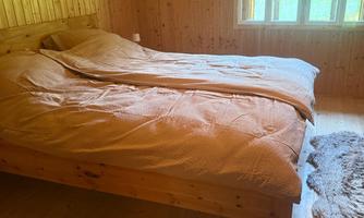 A cozy bedroom with a wooden bed and two beds. Bright wooden walls and large windows create a pleasant atmosphere.