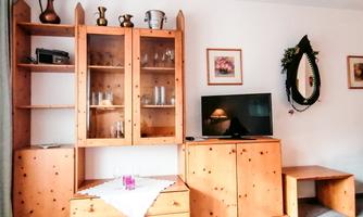 A cozy living room with wooden furniture and a television. The room is bright and cheerfully designed.