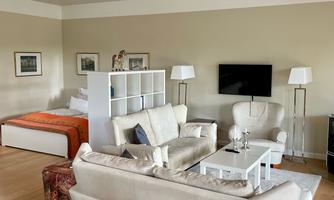 A modern living room with comfortable furniture and a television. There is a bright wooden floor and a cozy atmosphere.