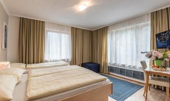 A cozy bedroom with two beds, bright curtains, and a table holding a small breakfast treat. The room is designed to be friendly and inviting.