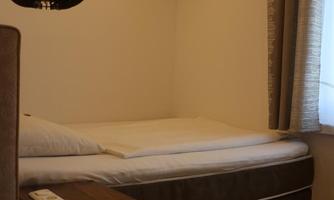 A simple bedroom with a bed and a nightstand. The walls are light, and a modern light hangs from the ceiling.
