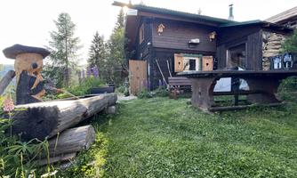 A rustic house surrounded by green meadows and trees. A wooden bench and a table invite you to linger.