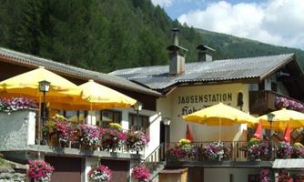A charming mountain cabin with yellow sun umbrellas and blooming flowers. In the background, green forests and mountains can be seen.