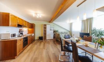 A modern kitchen with wooden cabinets and high-quality appliances. The open living area is bright and inviting, featuring a dining area and large windows.