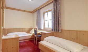 A simple room with two beds, a chair, and a windowsill. The walls are light, and the floor has a red carpet.