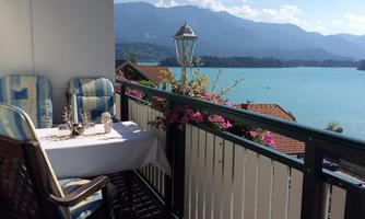 A cozy terrace with a view of a picturesque lake and the surrounding mountains. The table is beautifully set and surrounded by blooming plants.
