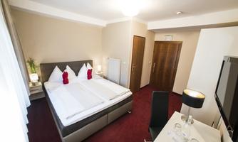 A cozy hotel room with a double bed and red carpet. There is a desk and modern furniture.