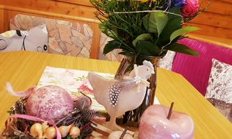 A beautifully set table with a bouquet of flowers, colorful decorative eggs, and stylish candles. The cozy wooden paneling in the background creates an inviting atmosphere.