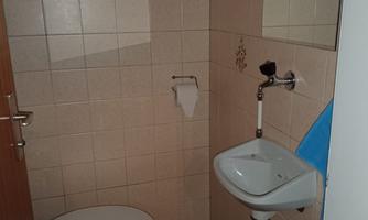 A small bathroom with a toilet and a sink. The walls are tiled and there is a towel in blue.