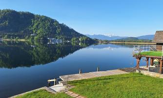 A tranquil lake with clear water and green shores. In the background, gentle hills and a blue sky can be seen.