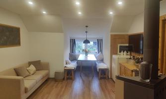 A modern living space with a beige sofa and a large dining table. The room has light walls and a cozy wood stove.