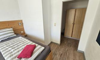 A simple room with a bed and striped bedding. In the background, there is a wardrobe and an entrance to another room.