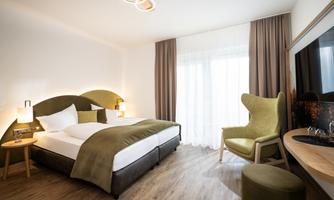 A modern hotel room with a large bed and cozy furniture. The room has plenty of natural light and a pleasant atmosphere.