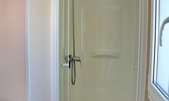 A modern shower cubicle with clean lines and a flexible showerhead. The room looks bright and inviting due to the window.