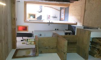 A cozy room with wooden shelves and a fireplace. The entrance leads to a bright room with additional furniture.