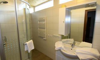 A modern bathroom with a shower and a sink. White tiles and towels create a clean atmosphere.