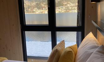 A cozy bedroom with a window that offers a view of a lake and mountains. The pillows are in warm shades of yellow.