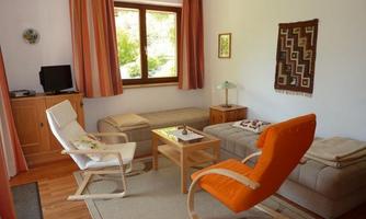 A cozy living space with large windows and plenty of natural light. There are comfortable seating areas and a small table in the middle.