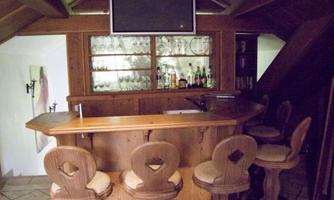 A cozy home bar with wooden shelves and four bar stools. In the background, glasses and bottles are visible, and a television hangs above the bar.