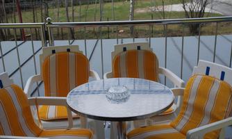 A balcony with four white chairs and a round table. The chairs have yellow-white stripes and the table has a glass top.