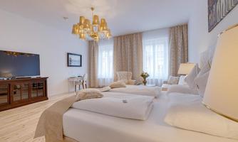 An elegant bedroom with bright walls and large windows. There is a modern bed, a television, and stylish furniture.