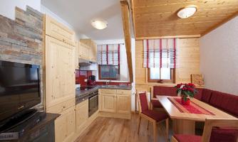 A cozy kitchen with wooden cabinets and modern appliances. The dining area is bright and inviting, with a red bench and a table.