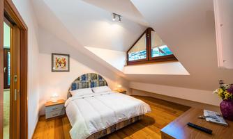 A cozy bedroom with slanted walls and a large bed. Large windows bring a lot of light into the room.