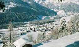 A snowy landscape with a small village in the valley. The mountains in the background are also covered with snow.