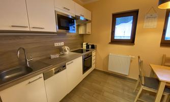 A modern kitchen with bright cabinets and a wooden floor. There is a dining table and windows that let in daylight.