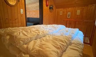 A cozy bedroom with wood paneling and a large bed. The bedding is white and the lighting is warm.