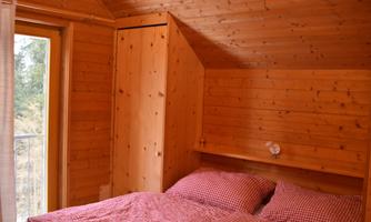 A cozy bedroom with wood paneling and a large window. The bed is topped with checked pillows and a blanket.