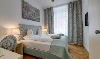 A cozy bedroom with two beds and a stylish headboard. The room has large windows that let in plenty of light and is tastefully decorated.