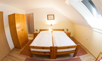 A cozy bedroom with two single beds and wooden furniture. The room has a bright atmosphere and a skylight.