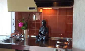 A modern kitchen with olive green cabinets and a stainless steel countertop. On the countertop, there is a Buddha statue and a flower vase with a pink flower.